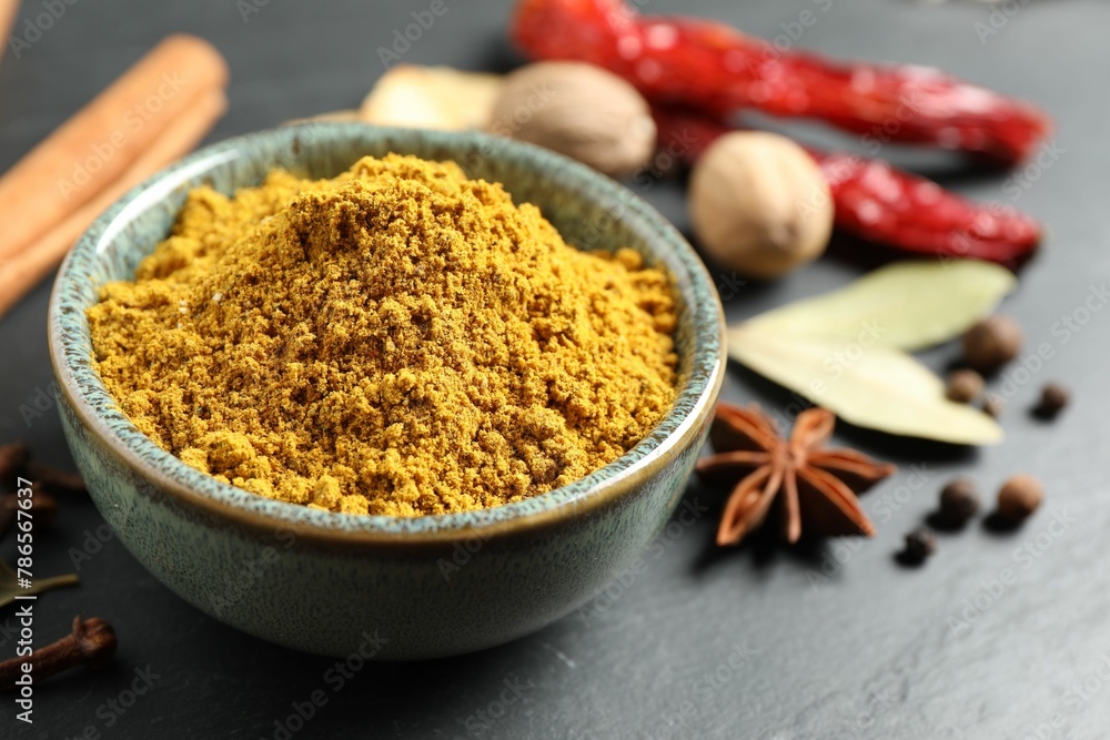 Dry curry powder in bowl and other spices on dark table, closeup