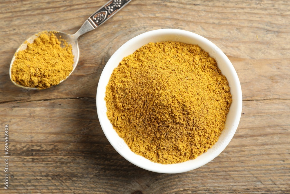 Dry curry powder in bowl and spoon on wooden table, top view Dry curry powder in bowl and spoon on wooden table, top view