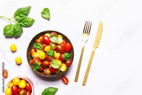 Bright juicy salad with colorful cherry tomatoes and aromatic basil leaves on white marble table top view. Healthy vegan food concept.