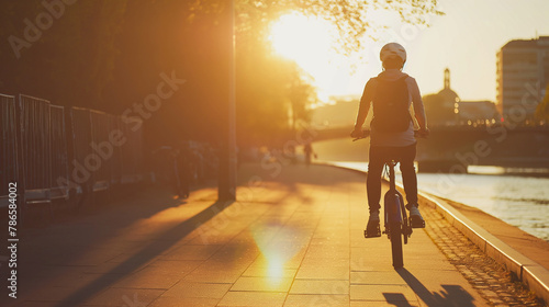 A young professional riding a stylish mini electric bike along a river promenade at sunset. The golden hour light creates long shadows and a picturesque backdrop, illustrating the photo