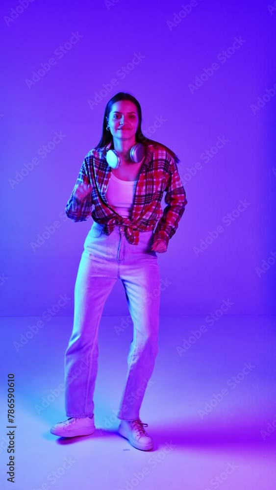 Full-length of young beautiful woman in casual clothes listening to music in headphones and dancing on blue studio background in neon light. Concept of human emotions, facial expression, lifestyle Full-length of young beautiful woman in casual clothes listening to music in headphones and dancing on blue studio background in neon light. Concept of human emotions, facial expression, lifestyle