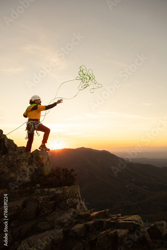 A person is standing on a mountain top, holding a green string. The sky is orange and the sun is setting