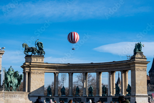 Red and white baloon with passengers rising high above Heroes Square and city park Varosliget in the city of Budapest, Hungary