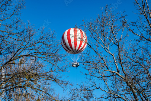 Red and white air baloon rising high above Budapest city park loaded with tourists observing hungarian capital from above