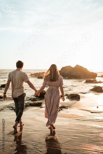 Backview portrait of beautiful young couple in love walking on the beach in California at sunset together, happy couple on vacation concept