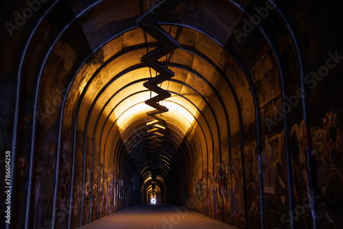 Obraz na płótnie Mysterious graffiti-filled tunnel with a spiraling walkway, illuminated by warm yellow light. w salonie