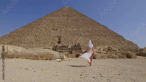 Back view of the young woman walking towards the Great Pyramids of Giza in Egypt and raising hands up. Tourist travel concept. 