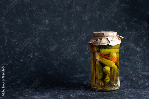 A jar with small cucumbers on a black shabby background. Daylight, selective focus with copy space