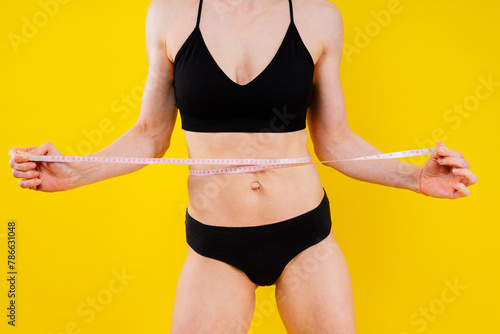 Athletic slim woman measuring her waist by measure tape after a diet over dark yellow background