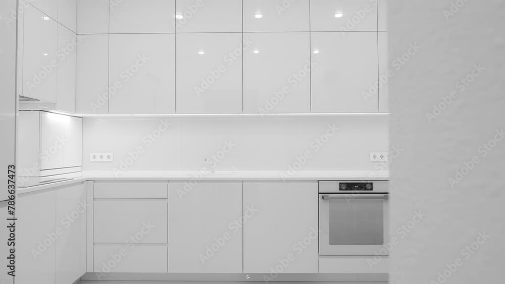 Front view of a modern luxury trendy snow white kitchen with many cabinets, glossy lacquered facades and integrated handle. Nobody Front view of a modern luxury trendy snow white kitchen with many cabinets, glossy lacquered facades and integrated handle. Nobody