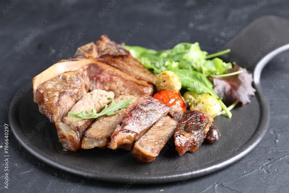 Delicious grilled beef meat, vegetables and greens on black table, closeup Delicious grilled beef meat, vegetables and greens on black table, closeup