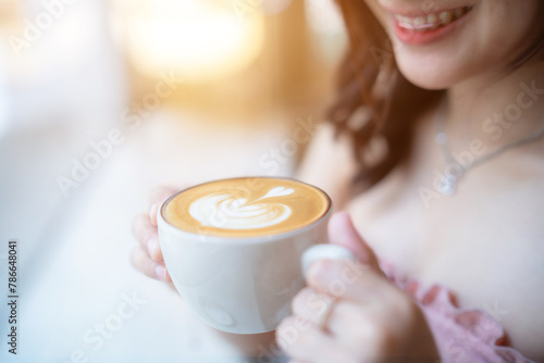 Close up holding Hot coffee latte with latte art milk foam in cup mug with happy Smiling woman relaxing sitting in cafe interior in coffee shop background,Business Lifestyle summer holiday concept