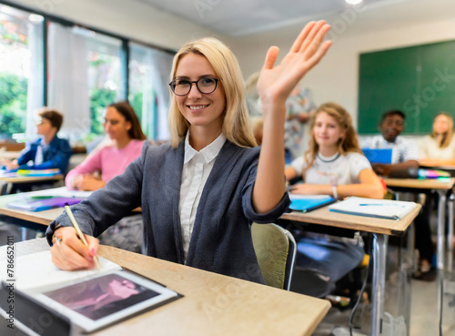 Smiling student at her desk raises her hand in classroom.