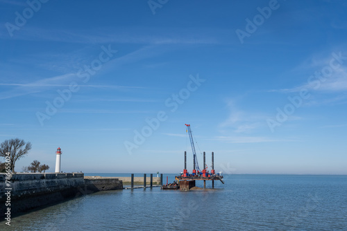 Barge dredging the harbor of saint martin de ré. white and red lighthouse next to it.