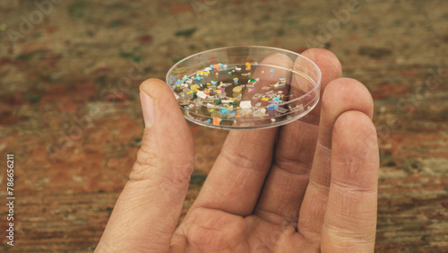 Close up shot of man holding a lab petri dish with microplastic particles. Concept of plastic pollution with nanoplastics. Detail of micro plastic particles that cannot be recycled.