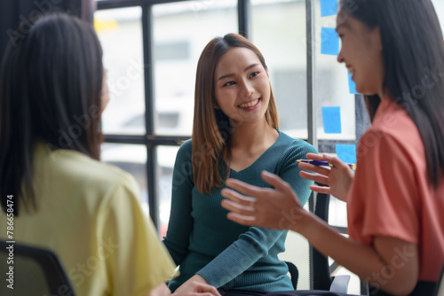 Asian businesswoman team in casual discussion with a focus on a smiling female professional. Collaborative teamwork and office interaction concept photo