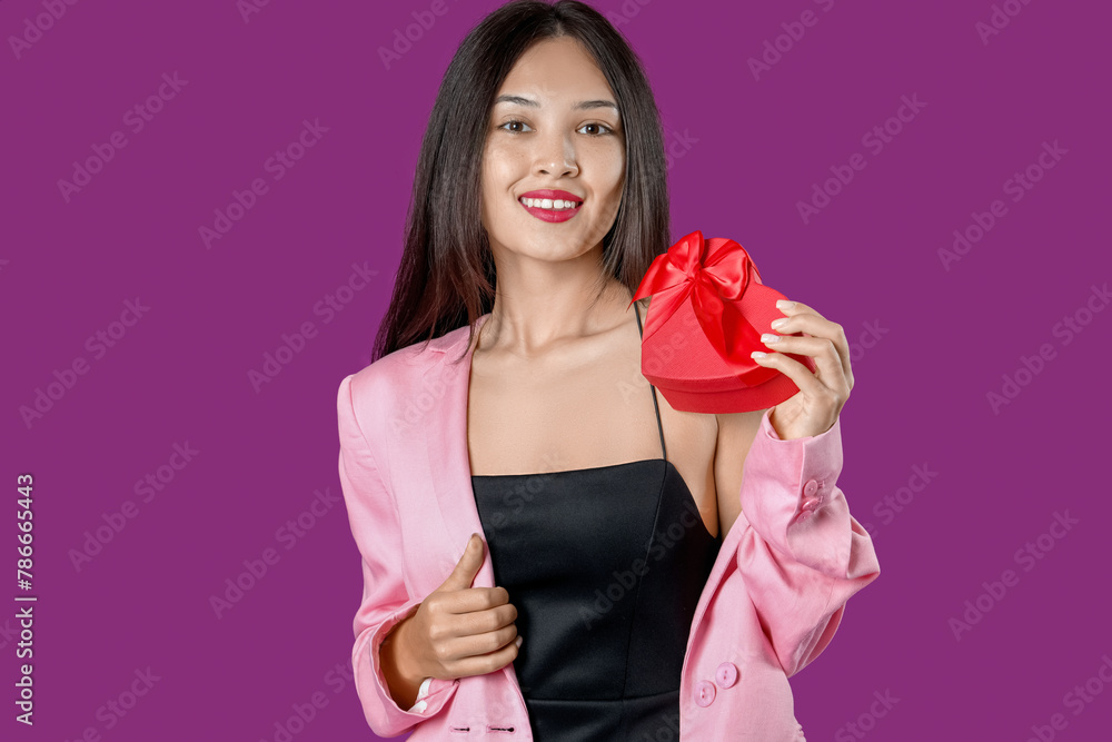 Beautiful young Asian woman with gift box for Valentine's Day on purple background Beautiful young Asian woman with gift box for Valentine's Day on purple background