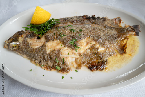 whole lemon sole fish cooked in butter on a white plate with a slice of lemon.