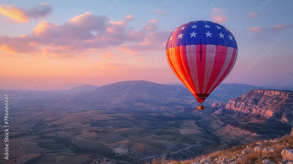 Hot air balloon with American flag design floats over scenic landscape at sunrise. Soft light bathes rolling hills and valleys below