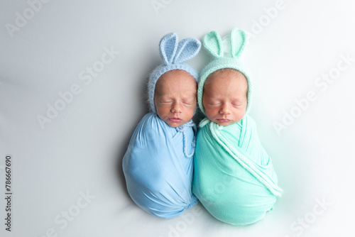 Tiny newborn twins boys in white cocoons on a white background. A newborn twin sleeps next to his brother. Newborn two twins boys hugging each other.Professional studio photography