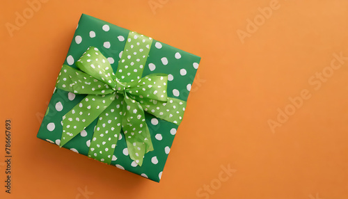 Saint Patrick's Day concept. Top view photo of green giftbox in wrapping paper with polka dot pattern and ribbon bow on isolated orange background with copy space 