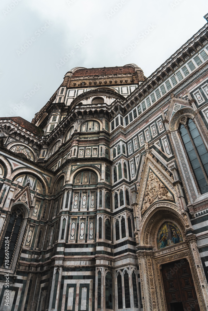 Santa Maria del Fiore Cathedral's ornate marble facade, blending Gothic and Renaissance styles, topped with its iconic dome. Stained glass windows and religious imagery adorn it under the cloudy sky. Santa Maria del Fiore Cathedral's ornate marble facade, blending Gothic and Renaissance styles, topped with its iconic dome. Stained glass windows and religious imagery adorn it under the cloudy sky.