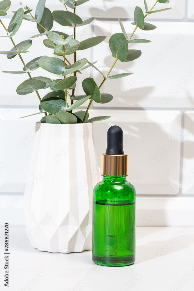 Green eucalyptus oil bottle with white vase and plant Green eucalyptus oil bottle with white vase and plant