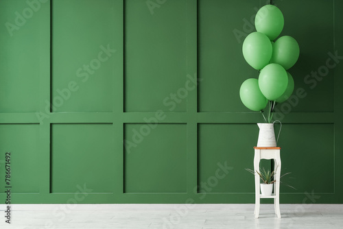 Vase with balloons on table near green wall