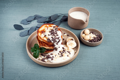 Traditional American Pancakes with banana honey cream, macadamia nuts and chocolate crumbles served as close-up on a Nordic design plate