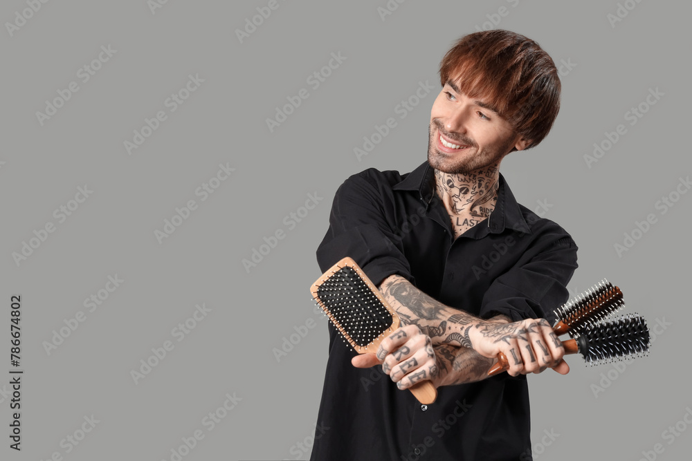 Fototapeta premium Young tattooed barber with hair brushes on grey background