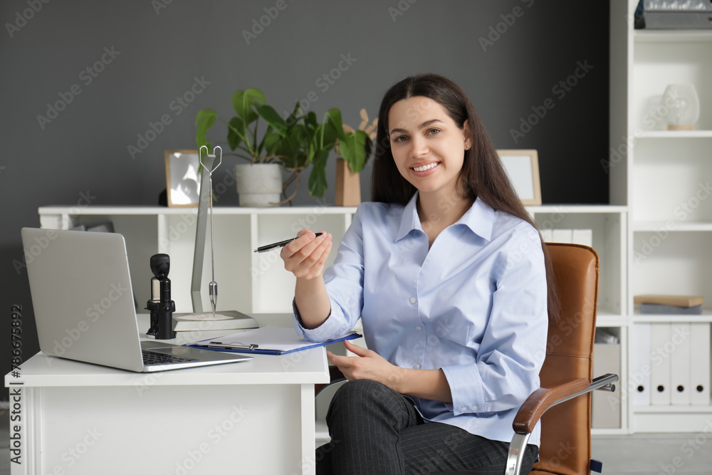 Pretty businesswoman sitting at table with laptop in light office Pretty businesswoman sitting at table with laptop in light office