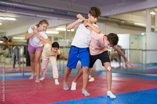 Pair of teenage boys practicing self-defense moves during group training in gym