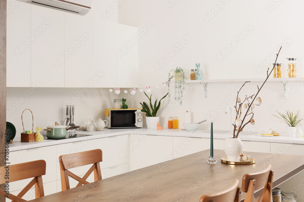 Vase with tree branches and Easter eggs on dining table in light kitchen