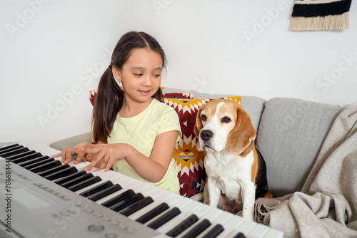 Cute little Asian girl with Beagle dog playing synthesizer at home