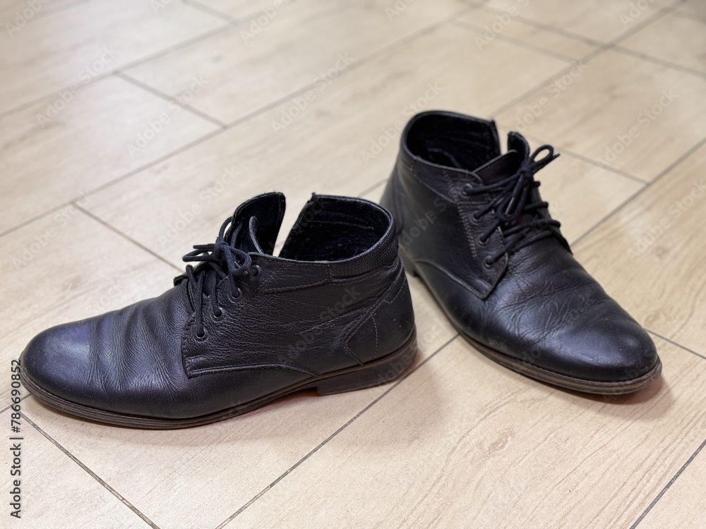 Old and dirty black lace-up shoes are on the ceramic tiles in the hallway of the house Old and dirty black lace-up shoes are on the ceramic tiles in the hallway of the house