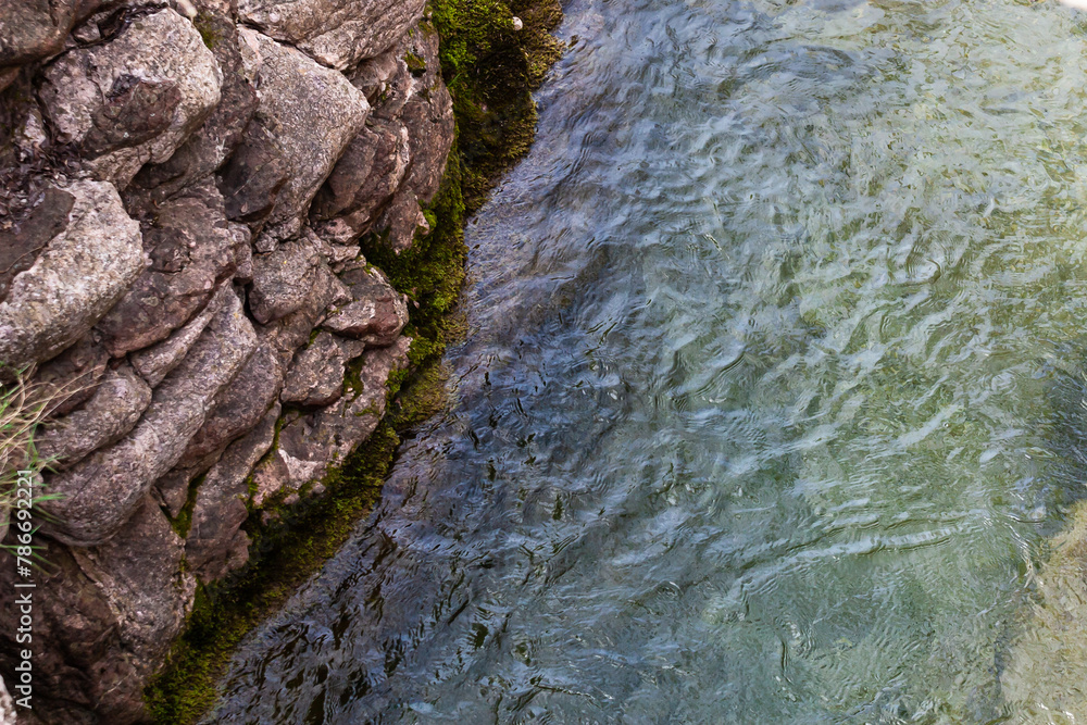 River flowing along a rocky cliff next to a waterfall, with moss and reflections in the water. View from above. Background. Texture. Horizontal. River flowing along a rocky cliff next to a waterfall, with moss and reflections in the water. View from above. Background. Texture. Horizontal.