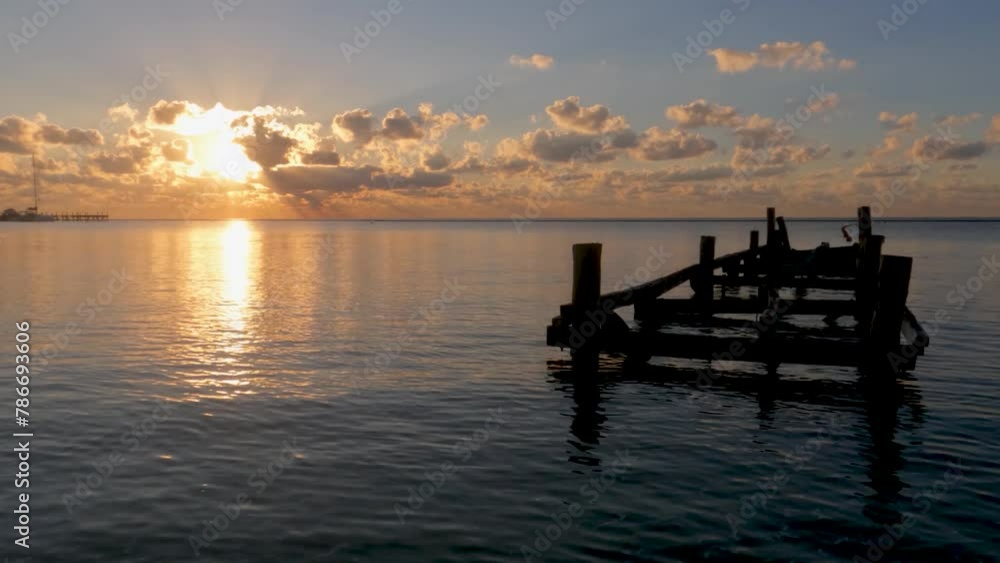 Sunrise over the water with golden sun ray peaking from behind the clouds over a backlit dock in the water Sunrise over the water with golden sun ray peaking from behind the clouds over a backlit dock in the water