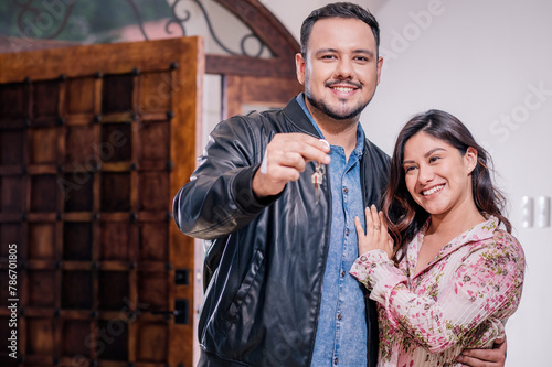 A young Hispanic couple shows a key with the image of a house on it. They bought a new house or apartment.