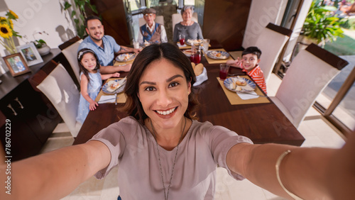 Canvas Print Beautiful Latin woman makes a selfie with her cell phone to keep the memory of grandparents, parents and grandchildren together at the table