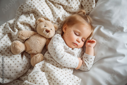 Cute little baby girl sleeps in her bed with toy teddy bear. View from above