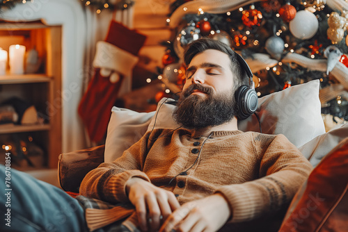 Handsome bearded man in headphones comfortably seated, leaning back, relaxing and listening to good music. Quiet and cozy Christmas celebrations at home