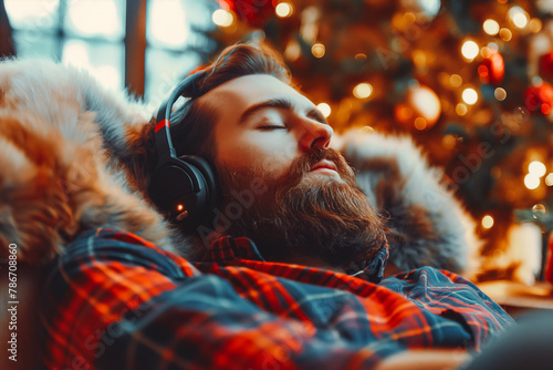 Handsome bearded man in headphones comfortably seated, leaning back, relaxing and listening to good music. Quiet and cozy Christmas celebrations at home photo
