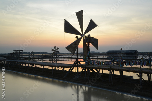 Sunset over the wooden turbines used to push seawater up into the salt fields during the hot summer months of Thailand, a beautiful landscape of the salt fields. Traditional salt farming culture.