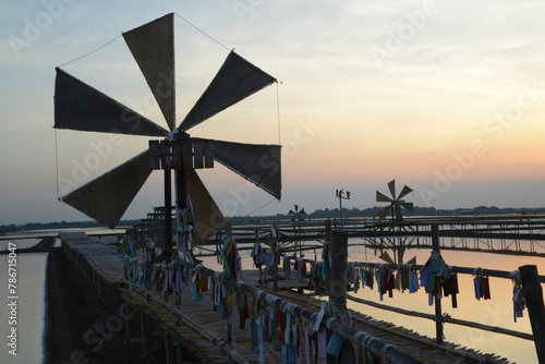 Sunset over the wooden turbines used to push seawater up into the salt fields during the hot summer months of Thailand, a beautiful landscape of the salt fields. Traditional salt farming culture.