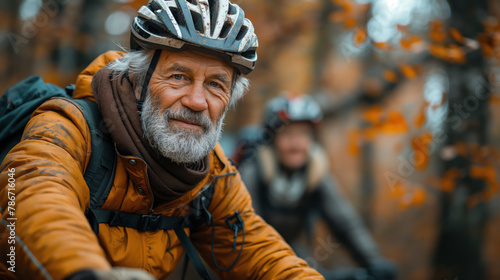 In the image, there is an elderly man wearing a helmet and a yellow jacket. He appears to be outdoors, possibly on a biking trail, with autumn foliage in the background.
