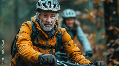 The image depicts a senior man wearing a cycling helmet and a brown jacket, riding a bike in a forest. He has a gray beard and a cheerful expression on his face. 