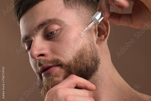 Fototapeta Naklejka Na Ścianę i Meble -  Handsome man applying serum onto his face on brown background