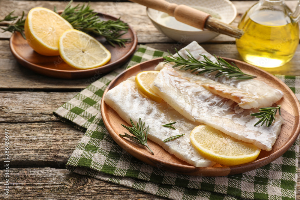 Fresh raw cod fillets with rosemary and lemon on wooden table
