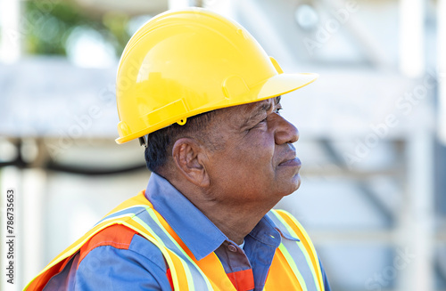 Portrait of elderly Asian male architect wearing a safety vest and yellow helmet at a construction site, side view