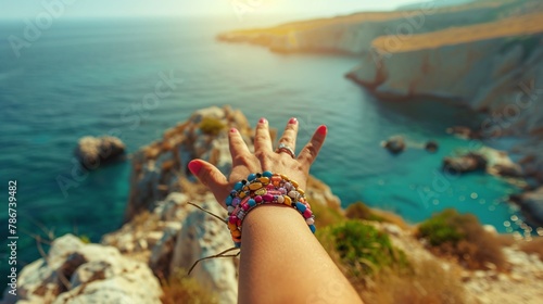 A traveler girl's hand adorned with bracelets pointing towards the sea on a sunny day. photo